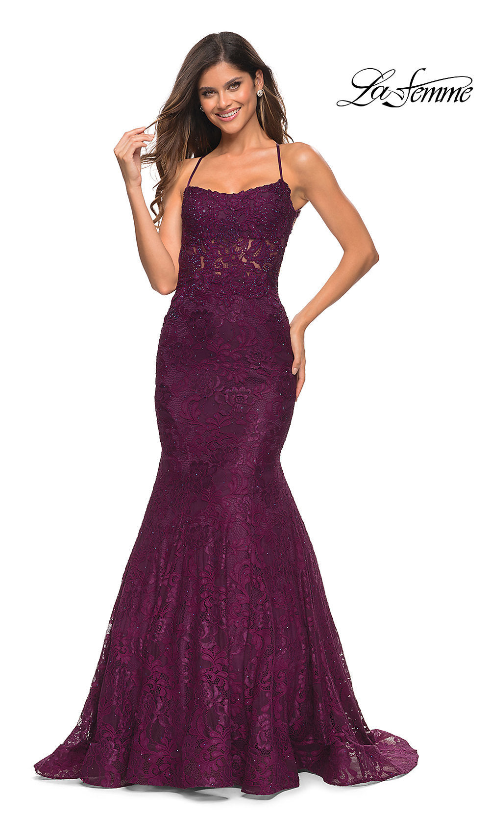 A woman stands smiling in a fitted, floor-length Open-Back Long Lace Mermaid Prom Dress by La Femme in Dark Berry, featuring thin straps and a slight mermaid silhouette. The La Femme logo is visible in the corner.